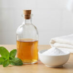 Bouteille en verre, bol de bicarbonate et feuilles de menthe sur une table en bois dans une salle de bain.