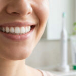 Gros plan sur le sourire d'une femme avec une brosse à dents et du dentifrice en arrière-plan flou.