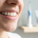 Gros plan sur le sourire d'une personne avec une brosse à dents et du dentifrice flous en arrière-plan.