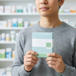 Un homme en pharmacie tenant une boîte de médicament vide pour le sevrage tabagique devant des étagères remplies.