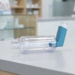 Chambre d'inhalation avec inhalateur bleu posée sur un comptoir dans une pharmacie.