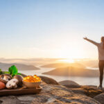Un plateau d'aliments riches en vitamine D (saumon, champignons) et gélules avec une personne au sommet face au soleil.