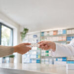 Un pharmacien remet une plaquette de comprimés à une cliente au comptoir d'une pharmacie lumineuse.