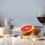 Un verre de vin, un pamplemousse coupé en deux et divers médicaments sur une table de cuisine.